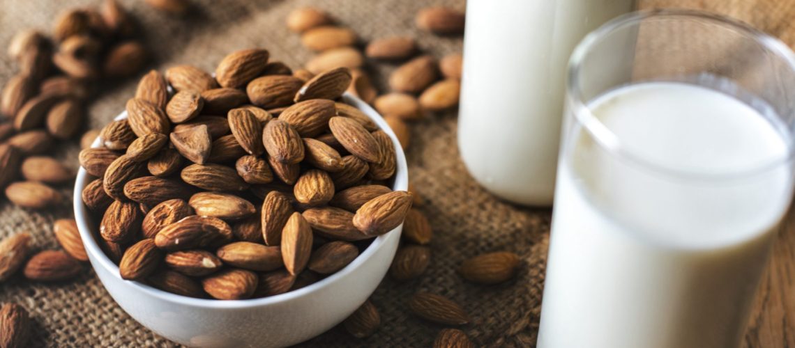 A white bowl of almonds and a glass of Almond milk
