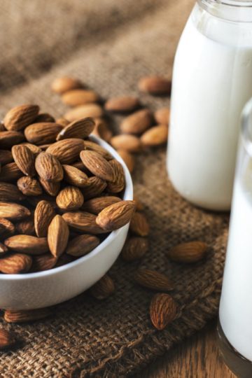 A white bowl of almonds and a glass of Almond milk