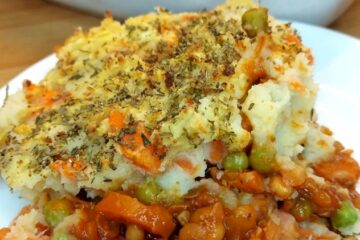 Portion of vegan shepherd’s pie on a white plate with rest of pie in the background