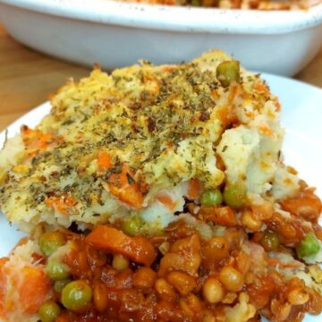 Portion of vegan shepherd’s pie on a white plate with rest of pie in the background