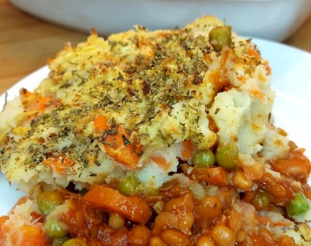 Portion of vegan shepherd’s pie on a white plate with rest of pie in the background