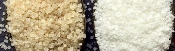 A spoon with white sugar and a spoon with brown sugar