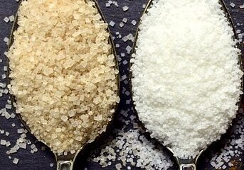 A spoon with white sugar and a spoon with brown sugar