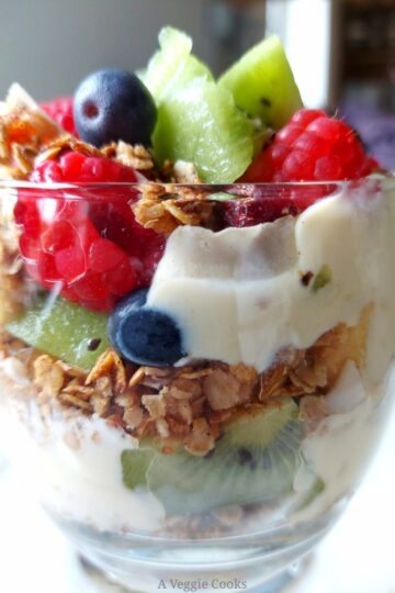 Fruit, yogurt and granola layer in a glass making Vegan Granola parfait