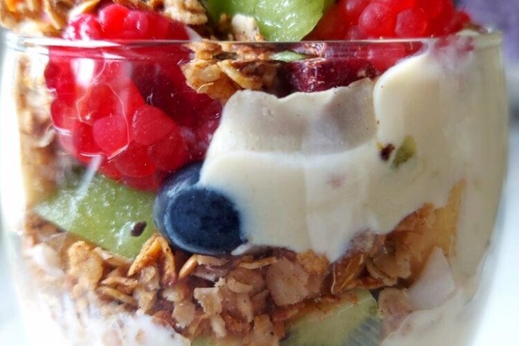 Fruit, yogurt and granola layer in a glass making Vegan Granola parfait